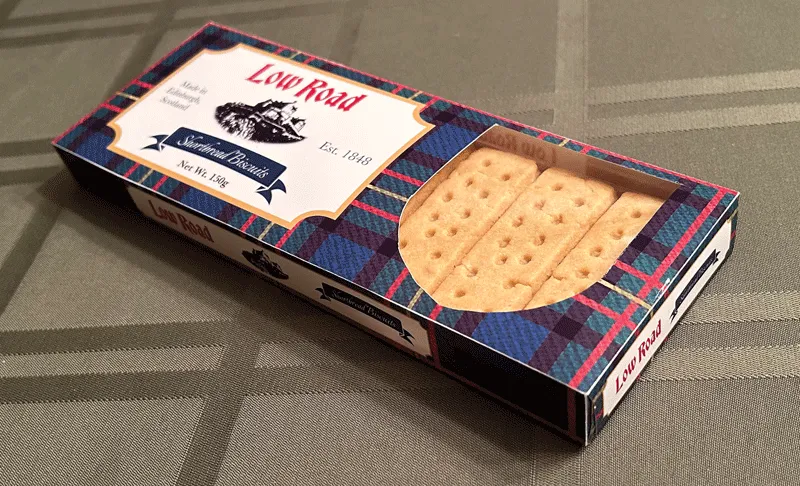 Low Road shortbread box with a shield shaped die cut revealing the biscuits inside sitting on tablecloth. 