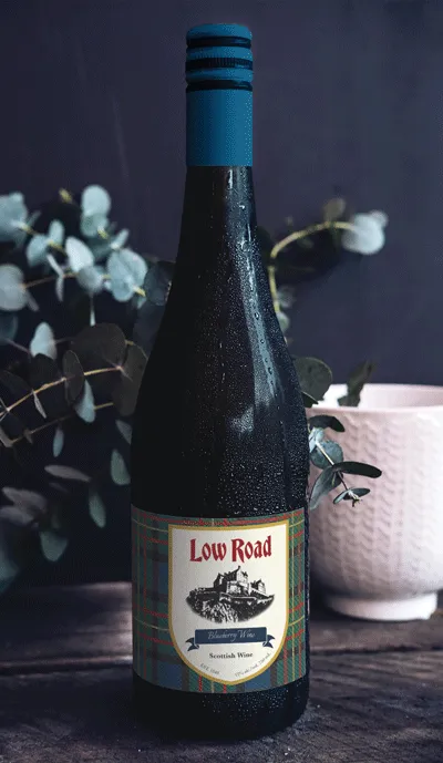 Label on wine bottle. It has a blue tartan pattern background with a shield in the canter containing the Low Road logo and wordmark.
